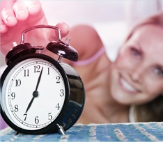 Foto di una sveglia con una donna sullo sfondo che allunga un braccio per spegnere la suoneria.